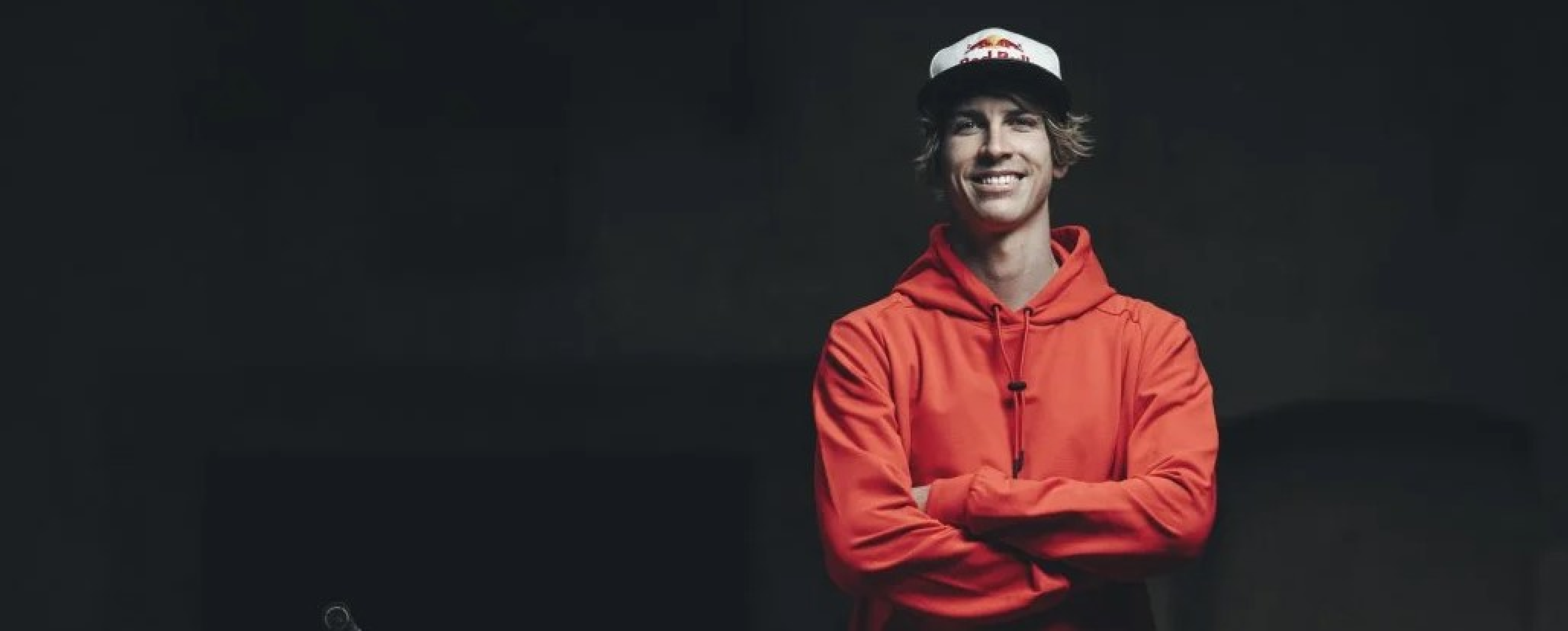Fabio prend la pose à côté de son vélo. Il a les bras croisé, porte une casquette RedBull et un hoodie rouge.