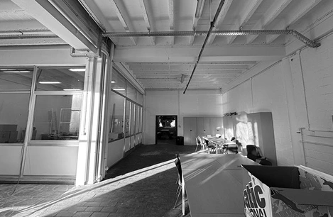 Image origanale en nuances de gris de la salle à réaménager. On voit que quelques tables et tables et chaises sont déjà présentes dans la salle.